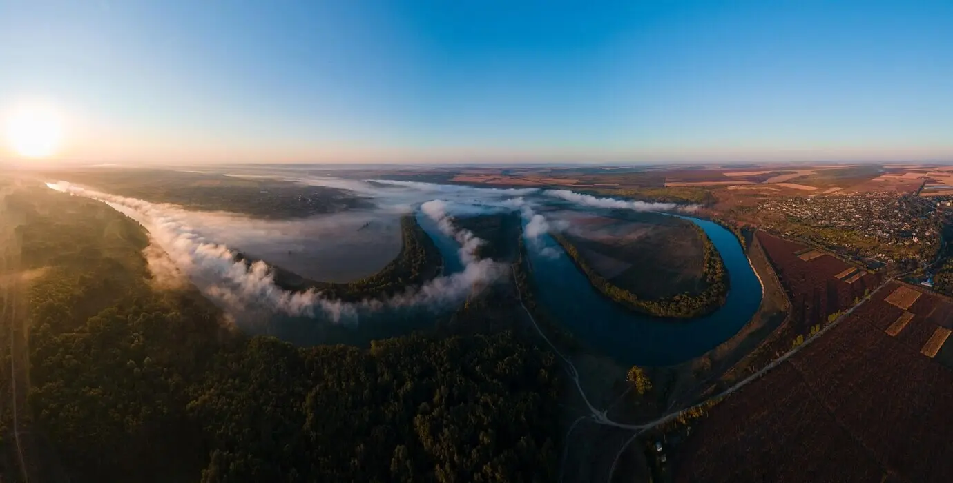 Vista panorámica aérea con dron de la naturaleza de Moldavia al amanecer: río con niebla, bosque y campos extensos.