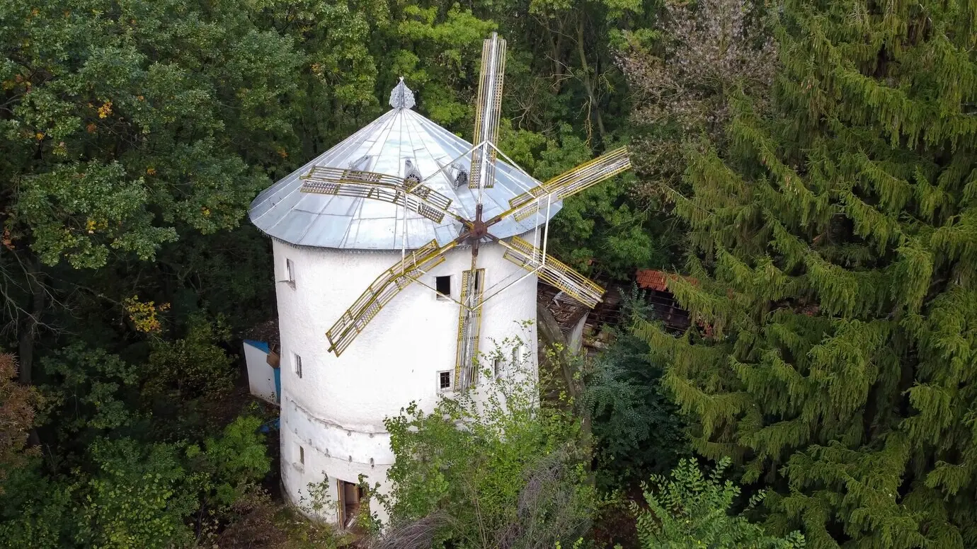 Vista aérea tomada con un dron de un molino de viento antiguo, rodeado de árboles verdes en un bosque de Moldavia.
